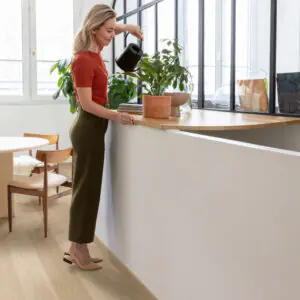 Light oak-effect vinyl plank floor in a bright room with a woman watering plants on a window ledge