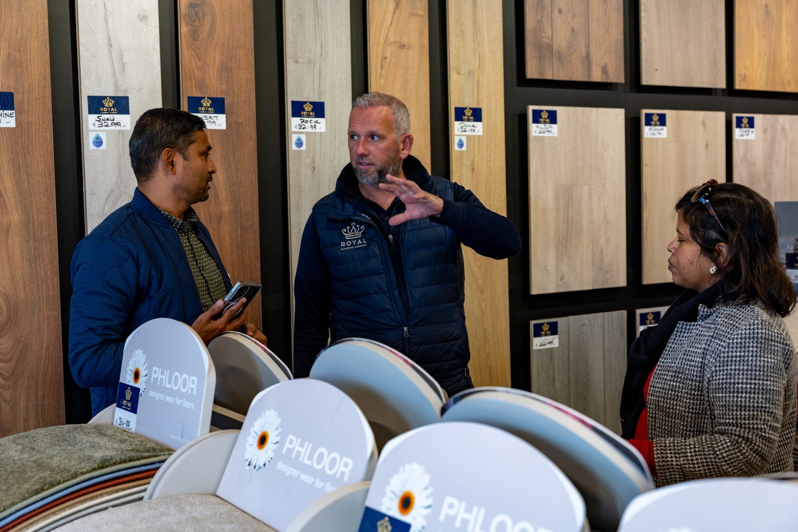 Royal Flooring Company staff advising customers beside an oak wood and LVT flooring wall display